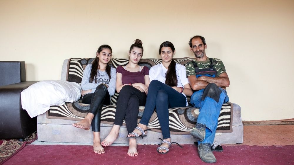 Ein alleinerziehender Vater sitzt mit seinen drei Töchtern auf einem Sofa.