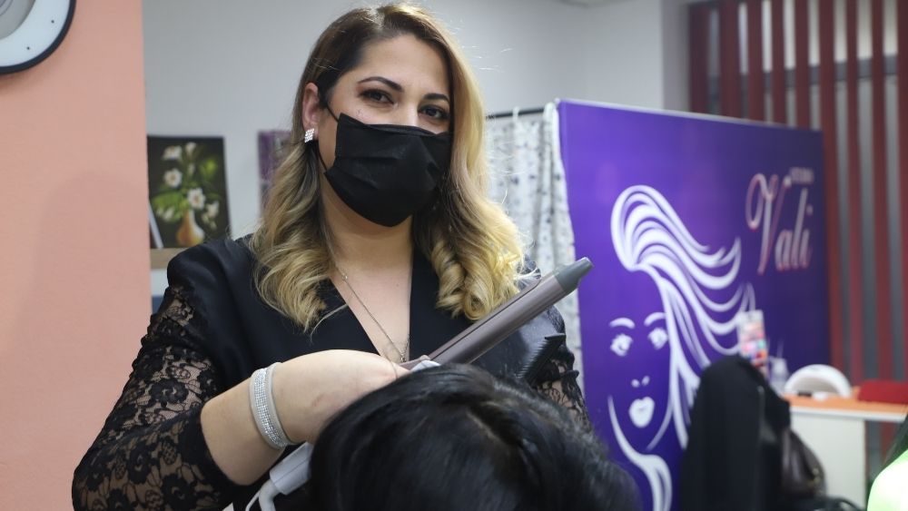 Eine Friseurin bearbeitet die Haare einer Kundin mit einem elektrischen Lockenstab.