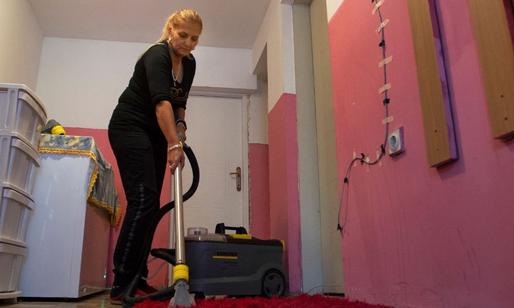 Eine Frau reinigt einen Teppich mit einem Staubsauger.