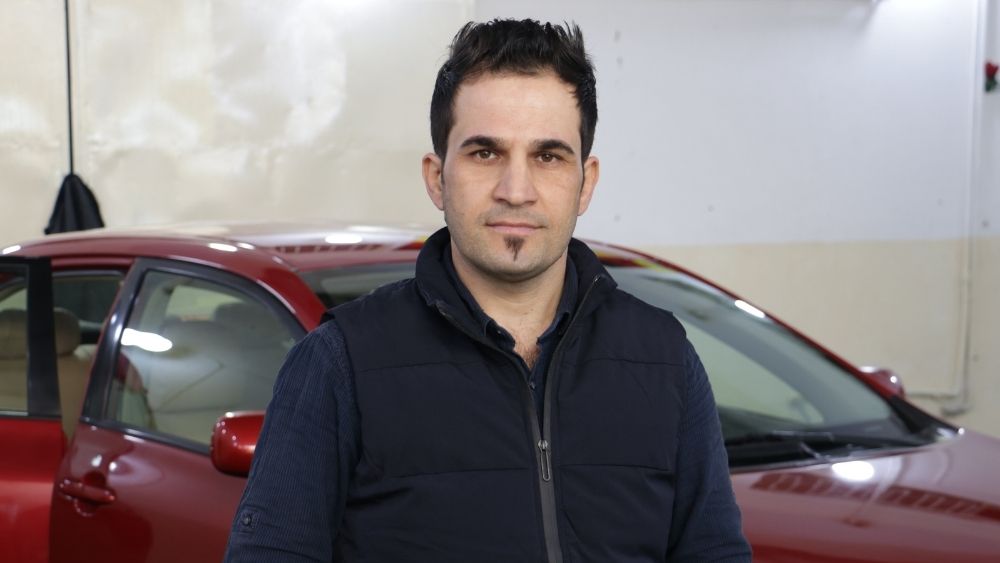 Ein Mann steht vor einem roten Auto und blickt in die Kamera.