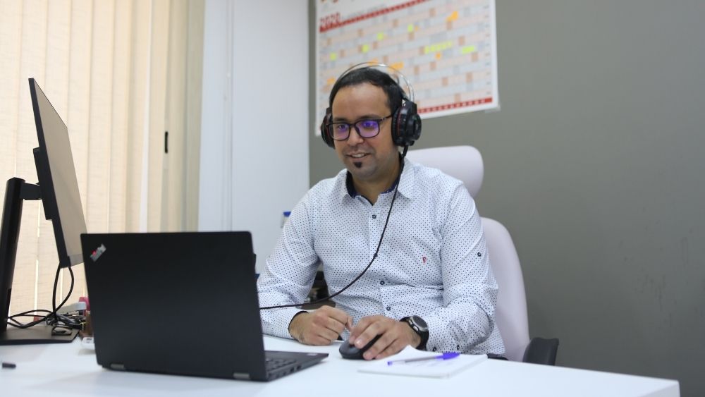 Ein Mann sitzt an einem Schreibtisch vor dem Computer. Er hat ein Headset auf.