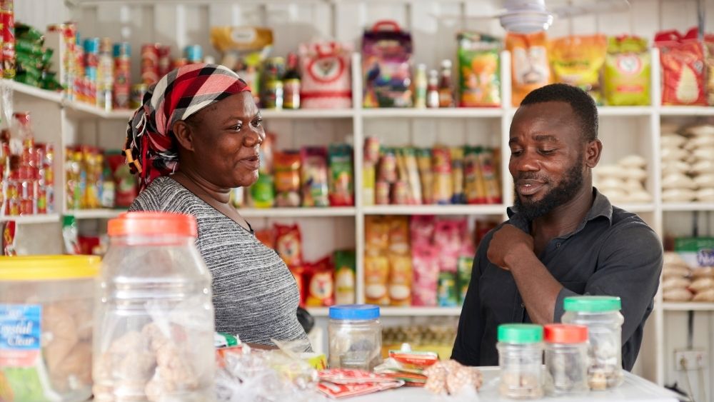 Ein Mann und eine Frau unterhalten sich und lachen. Im Hintergrund sieht man Lebensmittel in Regalen.