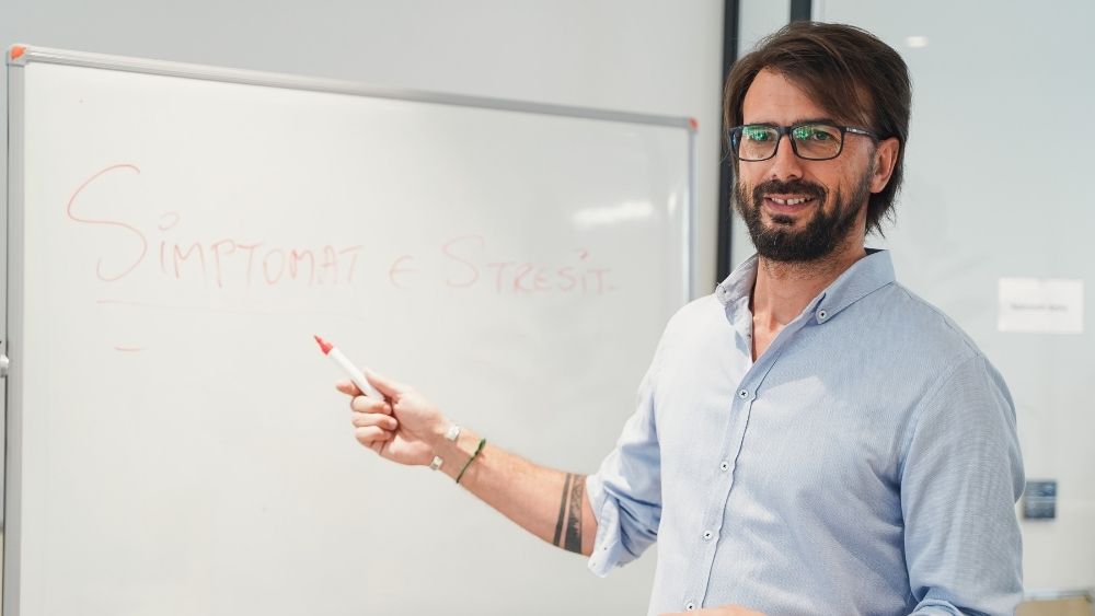 Ein Mann steht vor einem Whiteboard, auf das jemand „Stresssymptome“ geschrieben hat.