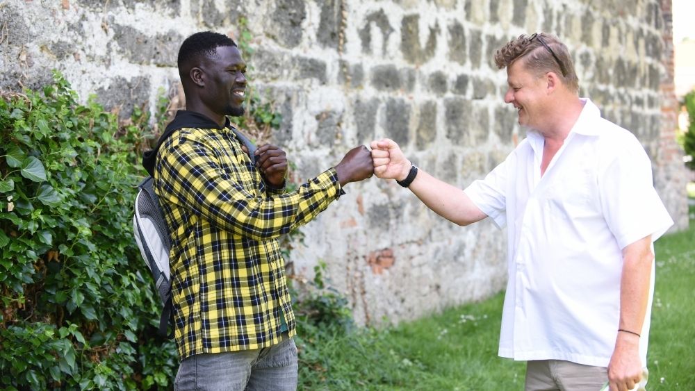 Zwei Männer stehen sich auf einer Wiese gegenüber und begrüßen sich per Handschlag.