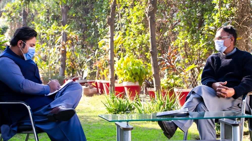 Beratungssituation: Zwei Männer sitzen an einem Tisch in einem Garten und unterhalten sich.