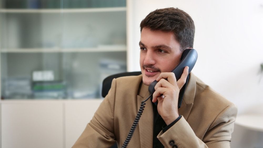 Ein Mann in einem Anzug sitzt an einem Schreibtisch und telefoniert.