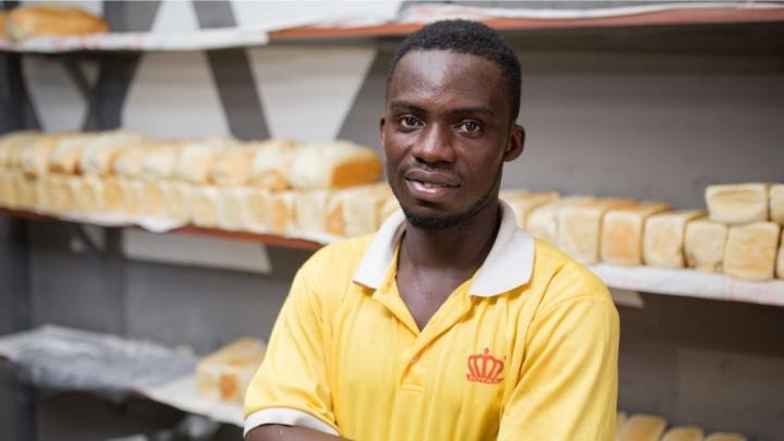 Ein Mann in einem gelben Shirt steht in einer Bäckerei. Im Hintergrund sind Brote zu sehen.