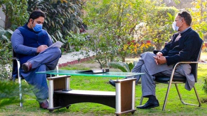 Zwei Männer sitzen sich in einem Garten an einem Tisch gegenüber.