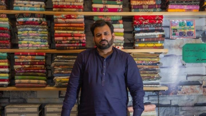 A man is standing in front of fabrics displayed in his shop.  