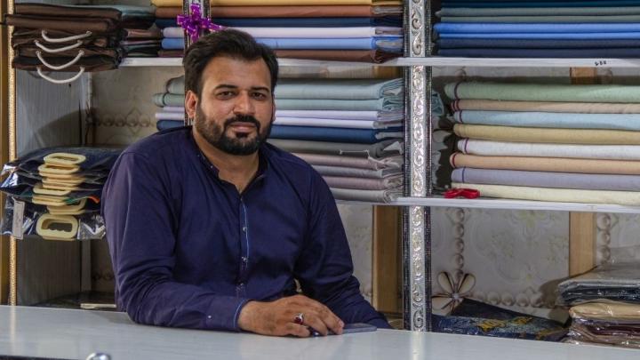 A man is sitting behind the counter in his fabric shop.