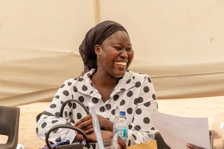 Eine junge Afrikanerin sitzt an einem Tisch, schaut auf die Seite und lacht. 