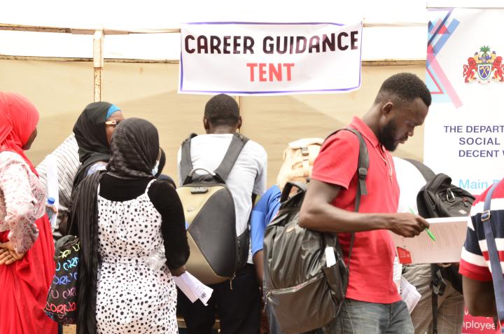 Eine Gruppe von Frauen und Männern steht vor einem Zelt an dem ein großes Schild mit der englischen Aufschrift: “Career Guidance Tent” übersetzt “Zelt für Berufsberatung” hängt.