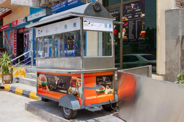 Ein leerer Imbisswagen mit angebrachter werbung für Burger und Wraps steht vor einem Gebäude. 