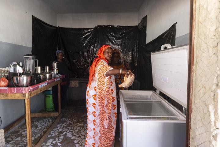 Frauen stehen in einer Küche, eine von ihnen holt ein Hähnchen aus einer Tiefkühltruhe.
