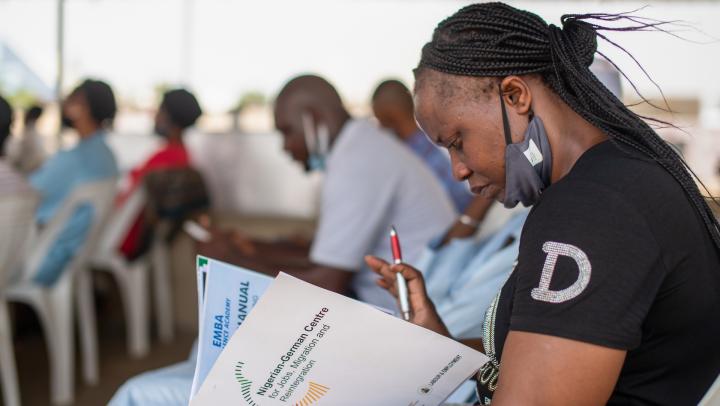 woman sitting in a conference looking into a broshure of the Nigerian-German Centre for Jobs, Migration and Reintegration