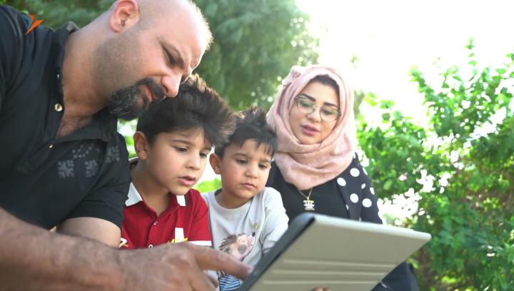 Taif schaut mit seinen beiden Söhnen und seiner Frau auf ein Tablet.