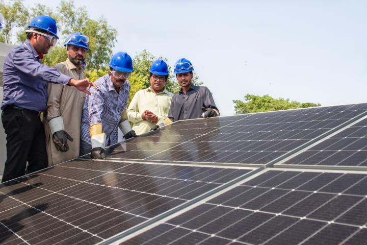 Eine Gruppe junger Männer steht an einem großen Solarmodul. 