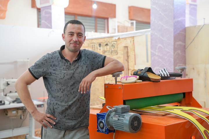  A man is standing at a machine that cuts out the soles of shoes. 