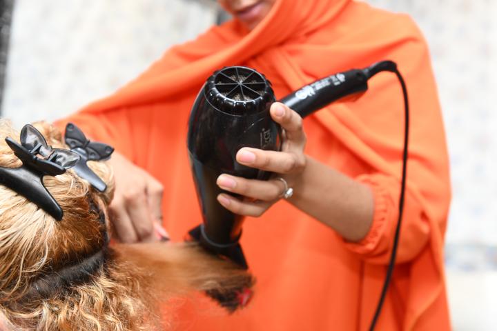  Une femme dont on ne peut pas reconnaître le visage sèche les cheveux d’une cliente au sèche-cheveux.   