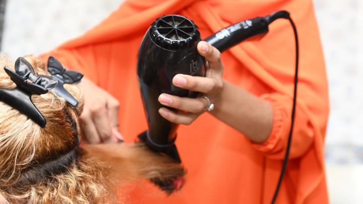 Eine Frau, deren Gesicht nicht zu erkennen ist, föhnt einer anderen Person die Haare. 