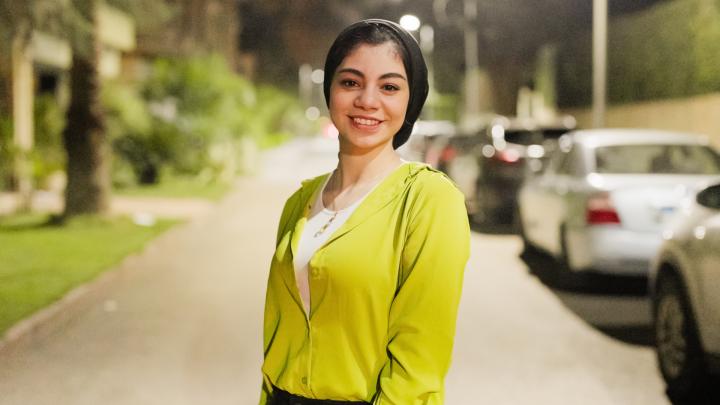 A young woman in a light green jacket looks into the camera and smiles. Video thumbnail