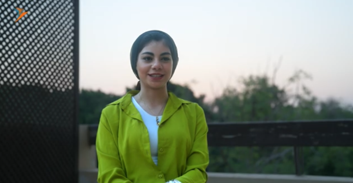  A young woman in a light green jacket looks into the camera and smiles. 